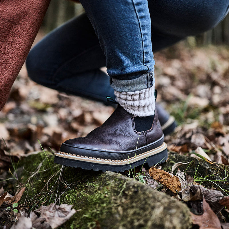 Person wearing dark brown boots with white soles on a natural background