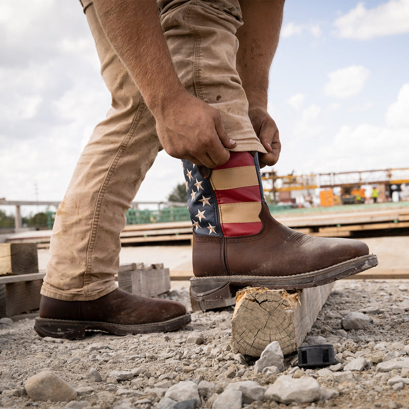 Person wearing brown work boots with American flag design on a construction site.