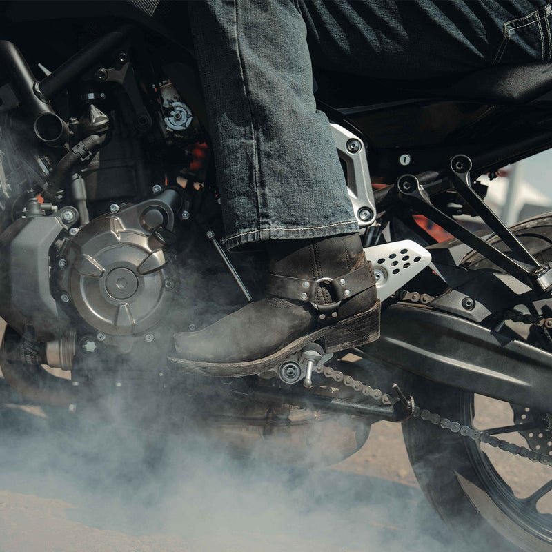 Close-up of a person's foot wearing a black Durango moto boot on a motorcycle with smoke in the background