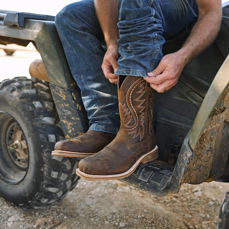Person wearing brown western work boots and blue jeans sitting on an ATV.
