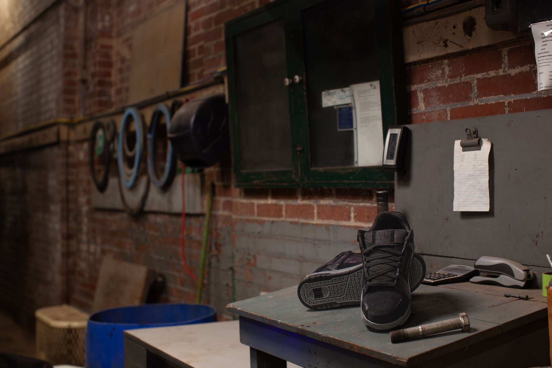 Pair of black high-top sneakers on a workbench in a workshop setting.