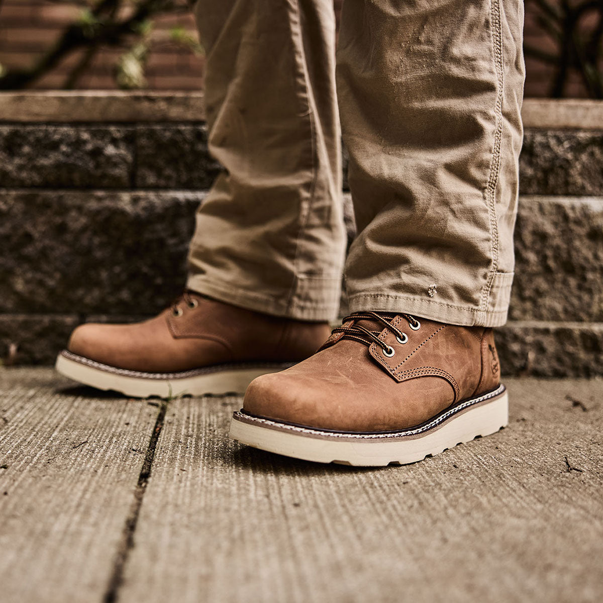 Brown leather boots with white soles worn by a person on concrete steps.