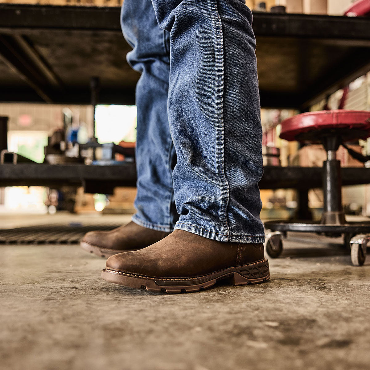 Person wearing blue jeans and brown work boots in a workshop setting